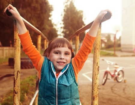 Portrait of a young girl hanging like monkey on the bar at the playground.の写真素材