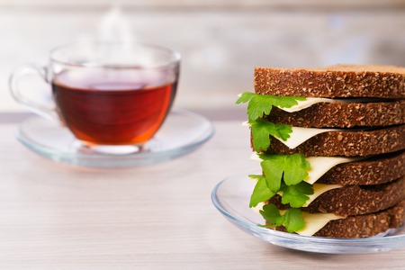 Bread with cheese and parsley and hot tea in a cup on the table.の写真素材