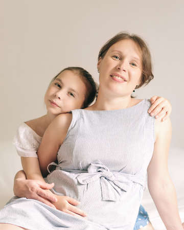 Beautiful pregnant woman and her cute little daughter are smiling while spending time together at...