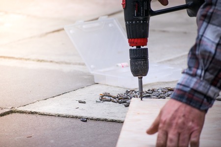 man screws piece of wood using an electric drill at home building wooden itemの写真素材