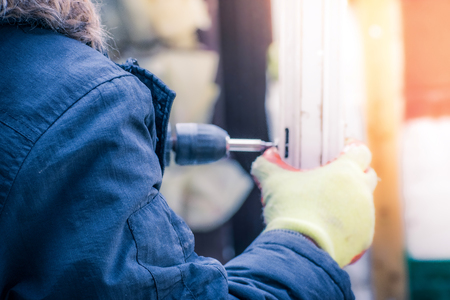 Closeup of Man wearing green gloves and Using a Power electric Drill screws and install a door using an electric drill at home in a clod winter dayの写真素材