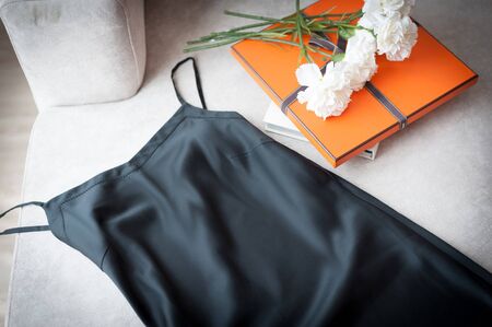 Black sexy satin pajama lay on nice looking elegance couch beside orange presents box and bouquetの写真素材