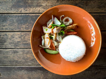 Grilled pork neck and cooked rice served in orange plate placed on wooden table - Famous Thai food...