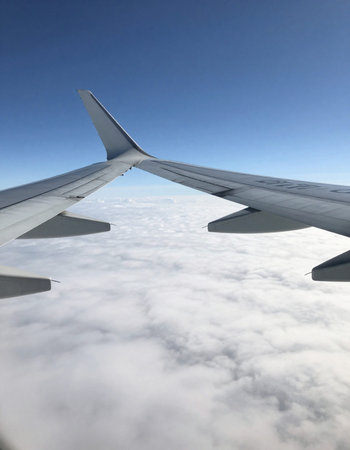 Wing of an airplane flying above the clouds in the blue sky.