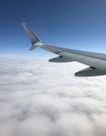 Wing of an airplane flying above the clouds, view from the window