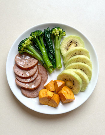sliced kiwi, broccoli and sausage on a plateの写真素材