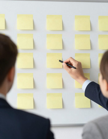 Businessman writing on sticky notes on wall in office, closeup