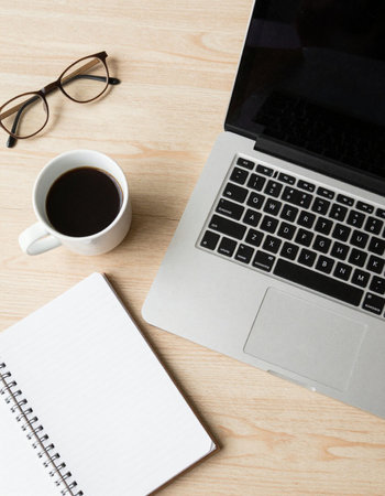 Laptop computer with coffee cup and notepad on wooden desk.