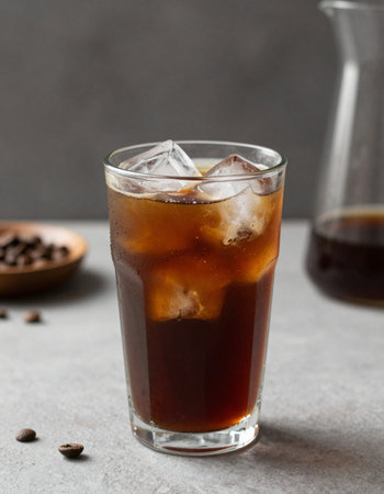 A glass of coffee with ice cubes and coffee beans on the table