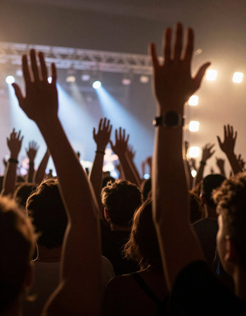 Crowd at a concert in front of a bright stage with hands raised