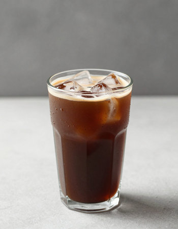 Iced coffee in glass on grey table, closeup. Space for text