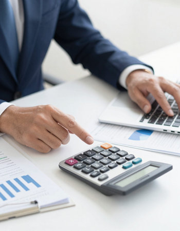 Businessman analyzing investment charts with laptop and calculator in office. Accounting