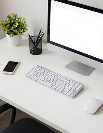 White office desk with computer, smartphone, stationery and plant.