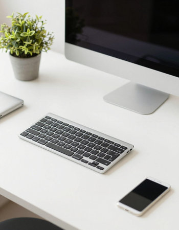 Working space with computer, mobile phone and plant on white table.