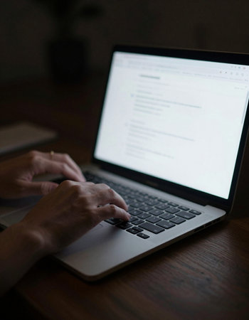 Close-up image of female hands typing on laptop keyboard at night