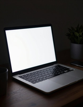 Laptop with blank screen on wooden table in dark room, stock photo