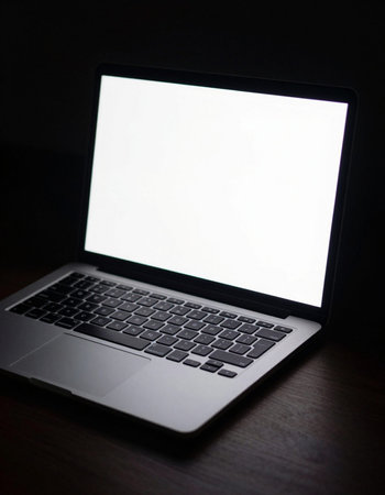 Laptop with blank screen on a wooden table in a dark roomの写真素材