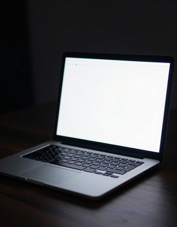 Laptop with blank screen on wooden table in dark room, stock photo