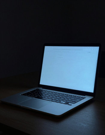 Laptop with blank screen on wooden table in dark room, stock photo
