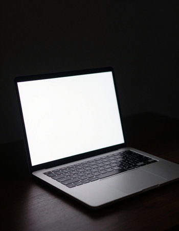 Laptop with blank screen on wooden table in dark room, stock photo