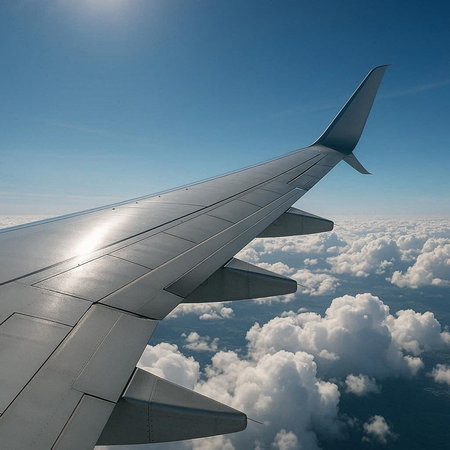 Wing of an airplane flying above the clouds on a sunny day.