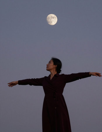 A woman in a long coat with a full moon in the background