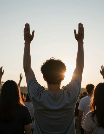 Back view of a young man raising his hands in the air at a music festivalの写真素材