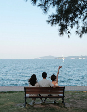 Back view of young couple sitting on the bench and looking at the sea