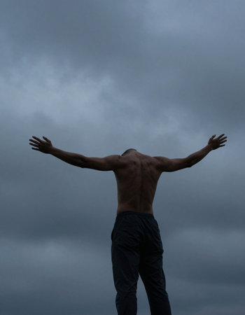 Man with torso exposed standing with arms outstretched against stormy sky
