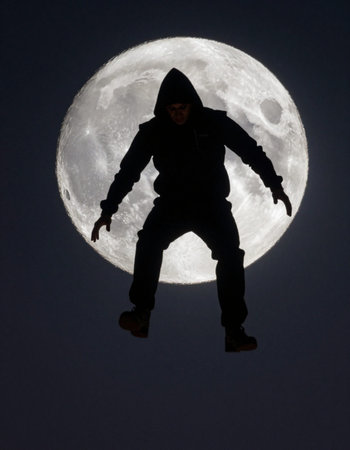 Hooded man jumping in front of a full moon in the night