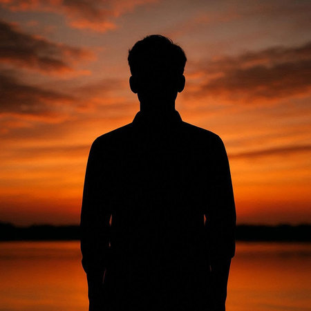 Silhouette of a man standing in front of a lake at sunset