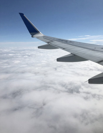 Wing of an airplane flying above the clouds in the blue sky.