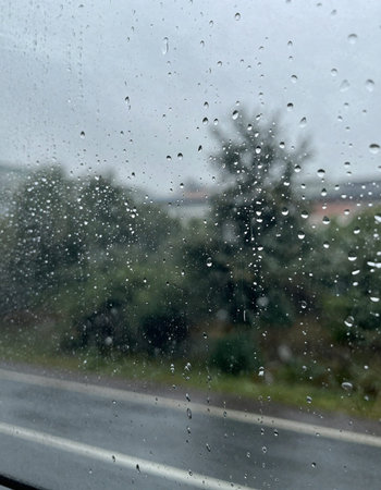 Rain drops on the window with a view of the road and the countryside