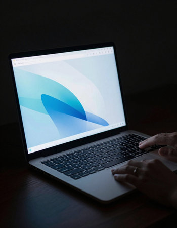 Hands typing on a laptop with a blue screen on a dark background