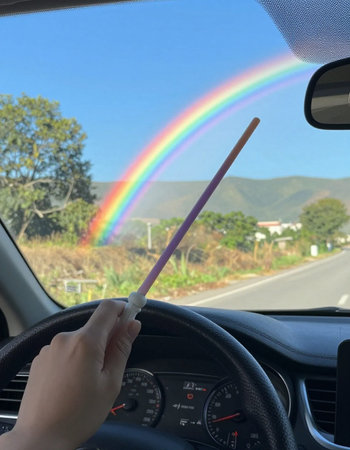 Driving a car with a rainbow in the sky behind the windshield
