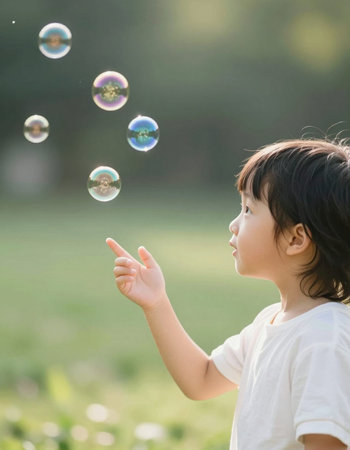 cute little asian boy playing with soap bubbles in the park