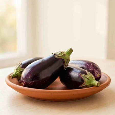 Eggplants in a clay plate on a wooden table.