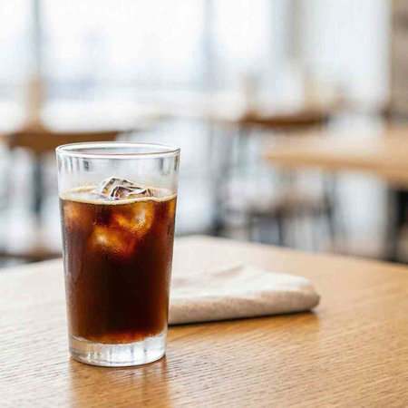Glass of cola with ice cubes on wooden table in coffee shop