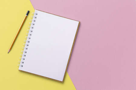 White notebook with pencils placed on pink and yellow background. Notebook concept.の写真素材
