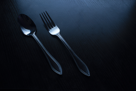 fork and spoon on a black table dark tone