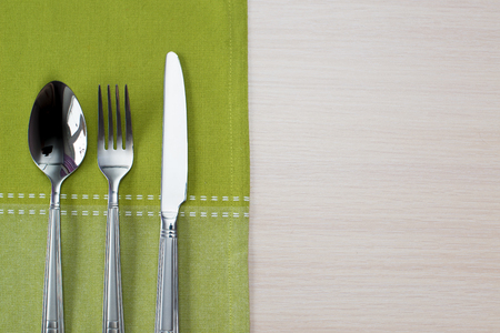 green napkin knife fork and spoon on a wooden tableの写真素材