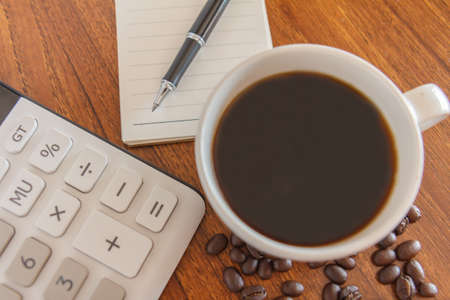 Blank notebook with pen,coffee and calculator on wooden table, business concep