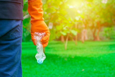 Volunteer man's hand picking up plastic bottle, clean up day, collecting waste on sea beach,...