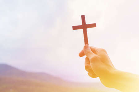 Man praying with cross, while holding a crucifix symbol with bright sunbeam on the sky.の写真素材