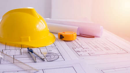 Yellow helmet and heap of drawing a project on a work desk. Project papers and tools beside. Free space in the middle. Flat lay, Construction background. Engineering tools. Copy spaceの写真素材