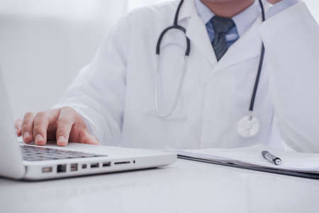Doctor working with laptop computer and writing on paperwork. Hospital background. Healthcare and medical concept. Focus on stethoscopeの写真素材