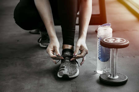 Woman tying shoe laces. Closeup of female sport fitness runner getting ready for jogging  in gym.の写真素材