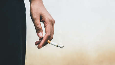 Man holding smoking a cigarette in hand. Cigarette smoke spread. dark background. Stop smoking cigarettes concept.の写真素材