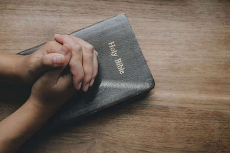 Woman with Bible praying, hands clasped together on her Bible on wooden table.の写真素材