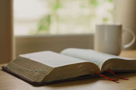 close up of open bible with a cup of coffee for morning devotion on wooden table with window light....